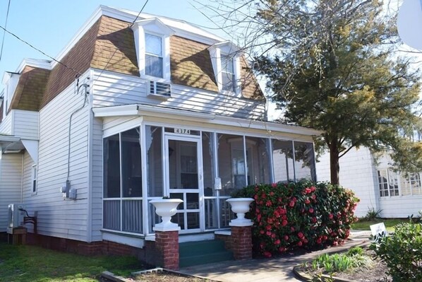 A two-story house with a covered porch, a number 4174, and a small garden with red flowers.
