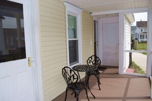 A covered porch with two metal chairs and a table, a white door, and a view of a residential street.