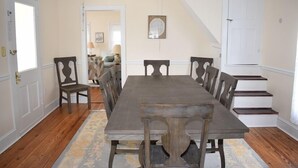A dining room with a large wooden table and chairs, a patterned rug, and a staircase leading to another room. - Sage House-Historic Downtown Location (Chincoteague)