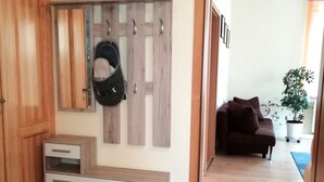 A room with a wooden cabinet, a coat rack with a bag, a brown sofa, and a potted plant.