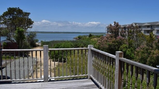 A wooden deck with a railing overlooking a body of water and a residential area. - Sailer Moon- 4 BR | Walk to Town | Sunset Views (Chincoteague)