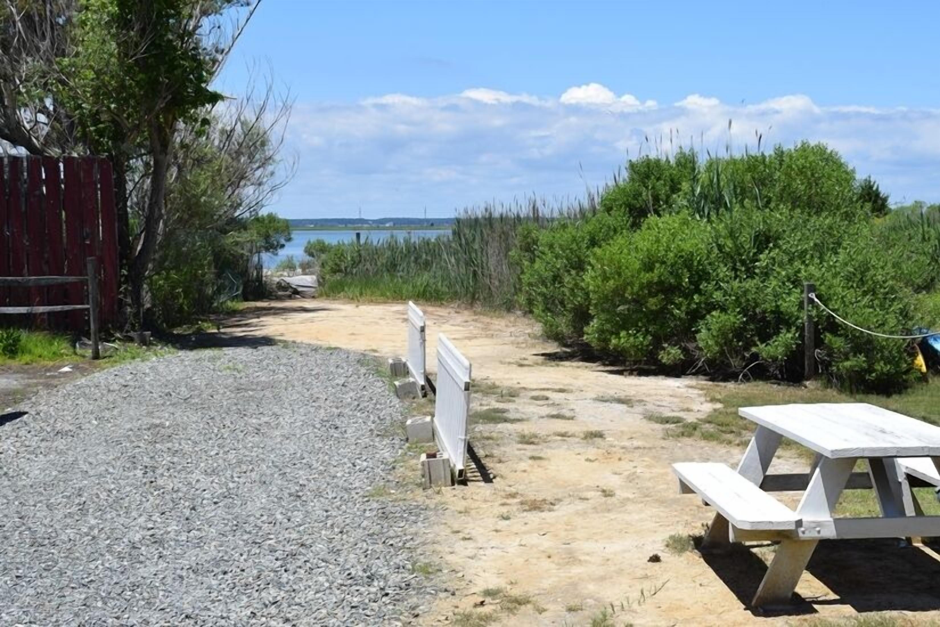 Un sendero de grava que lleva a una zona de playa con una mesa de picnic y una valla roja.