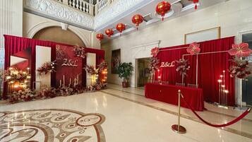 A grand hall with a red carpet, floral decorations, and a balcony with ornate railings.