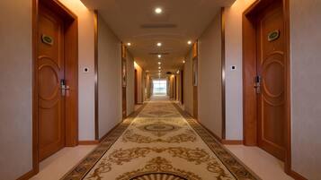 A hotel hallway with a patterned carpet, wooden doors, and recessed lighting.