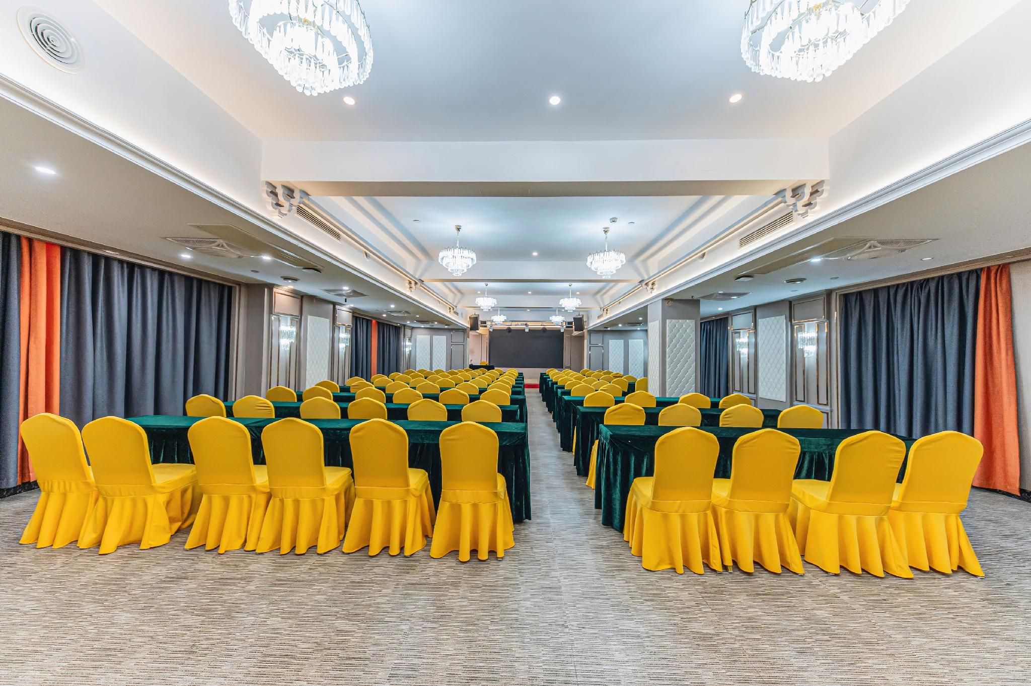 A conference room with rows of tables and chairs, chandeliers, and curtains.