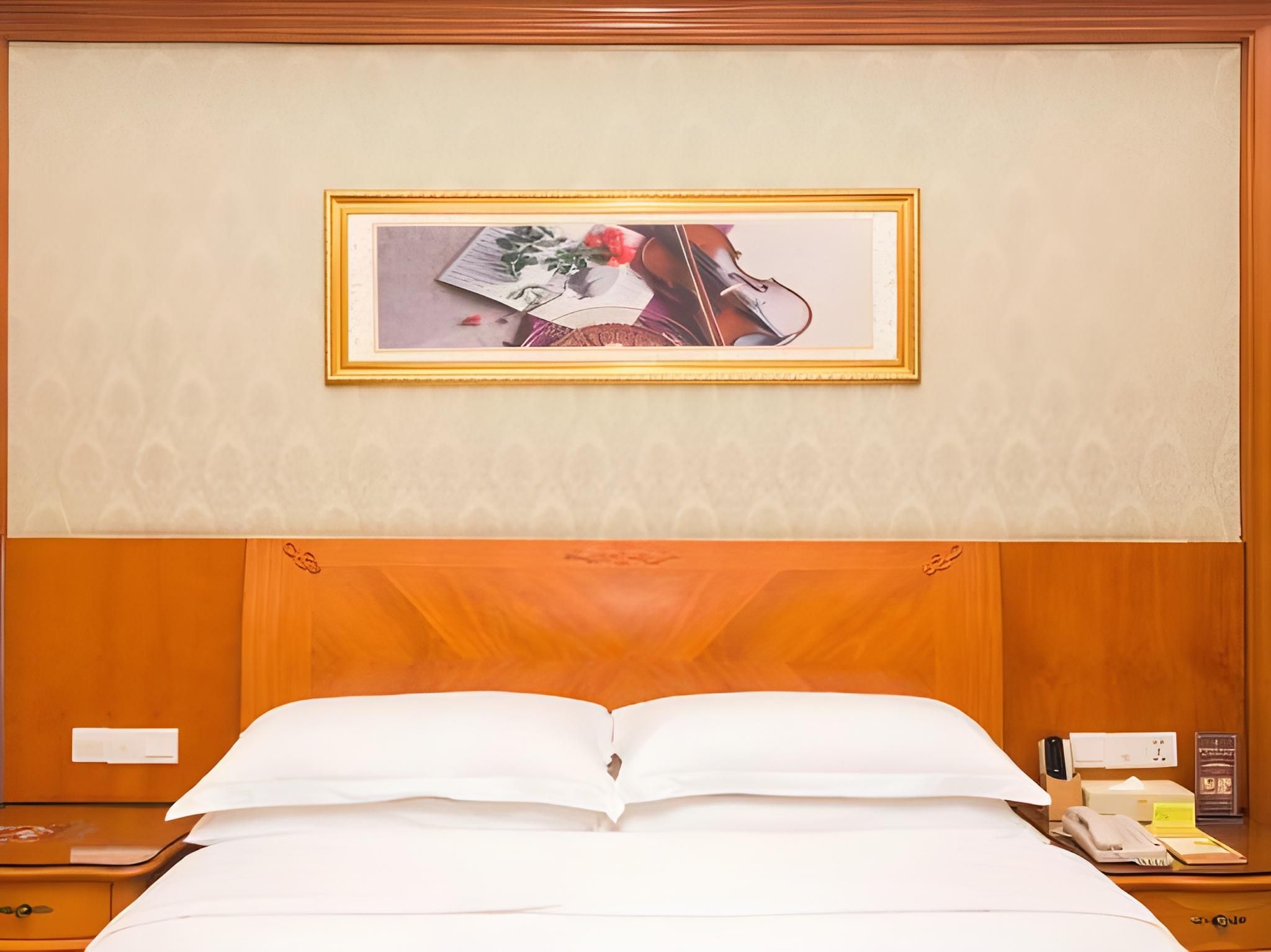 A hotel room with a large bed, a nightstand, a framed picture on the wall, and a wooden headboard.