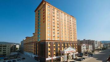 A multi-story hotel with a central entrance, parking lot, and surrounding buildings.