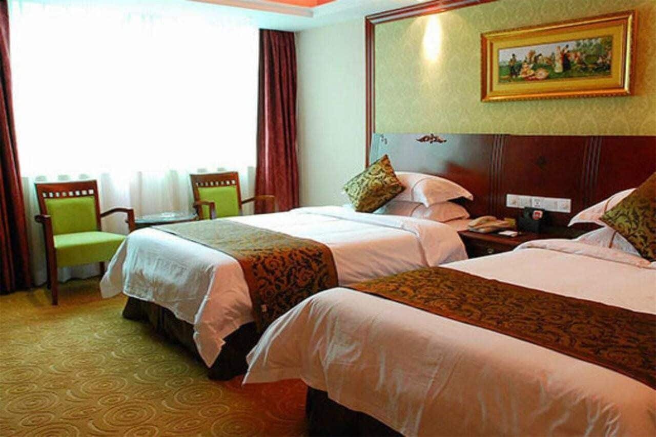 A hotel room with two beds, a desk, a chair, and a painting on the wall.