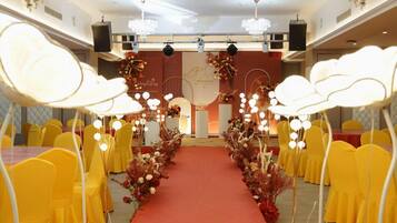 A banquet hall with rows of yellow chairs, a red carpet aisle, and floral decorations.