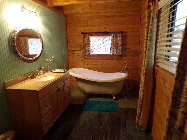 Un ba ño con paredes de madera, una bañera independiente, un tocador con espejo y una ventana con cortinas.