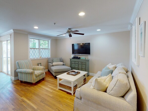 A living room with hardwood flooring, a ceiling fan, a television, a sofa, a chair, and a coffee table.