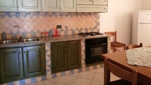 Una cucina con mobili verdi, un piano cottura a gas, un lavello e un frigorifero.