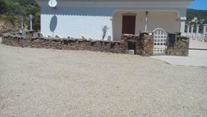 Un piccolo edificio bianco con tetto in tegole, un muro in pietra di fronte e un cancello.