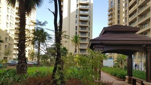 Un edificio residenziale con numerosi balconi, una zona esterna coperta con panche e un giardino curato con diverse piante e una palma.