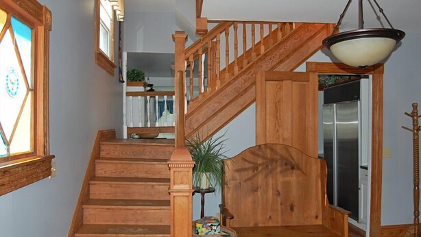 Eine Holztreppe mit einer Sitzbank am Fuß, einer Pendelleuchte und einer Tür zu einem Raum mit einem Kühlschrank.