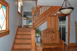 A wooden staircase with a bench at the bottom, a hanging light fixture, and a door leading to a room with a refrigerator.