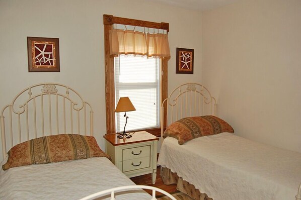 A bedroom with two single beds, a nightstand with a lamp, and a window with curtains.