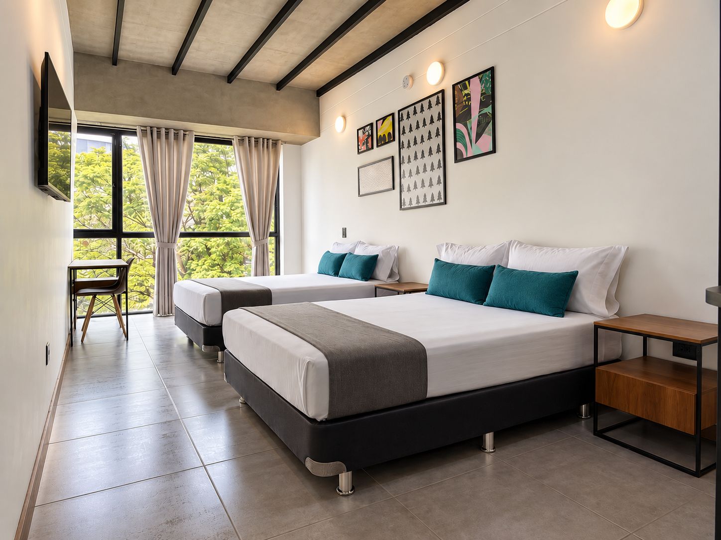 Quarto de hotel moderno com duas camas, uma escrivaninha e uma janela grande com cortinas.
