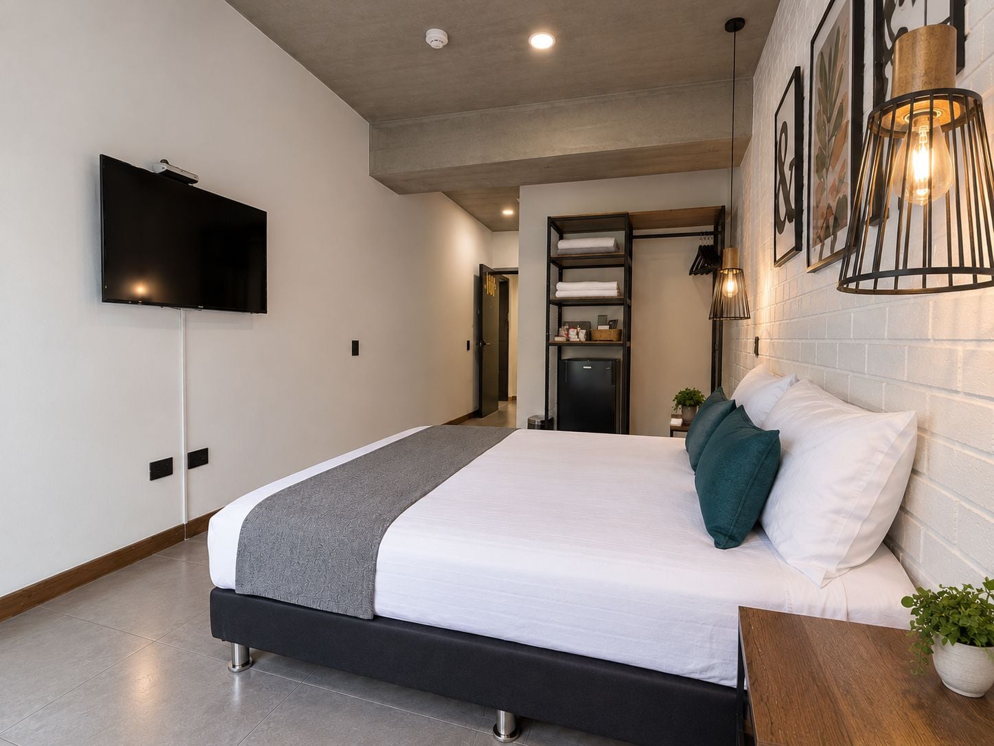 Quarto de hotel moderno com uma cama, televisão de tela plana, aquecedor embutido e uma pequena planta.