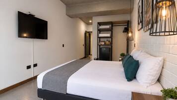 Quarto de hotel moderno com uma cama, televisão de tela plana, aquecedor embutido e uma pequena planta.
