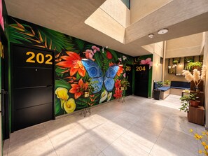 A hotel lobby with a vibrant floral mural, two black doors labeled 202 and 204, and a seating area with plants. - Hotel Loft 32 (Medellín)