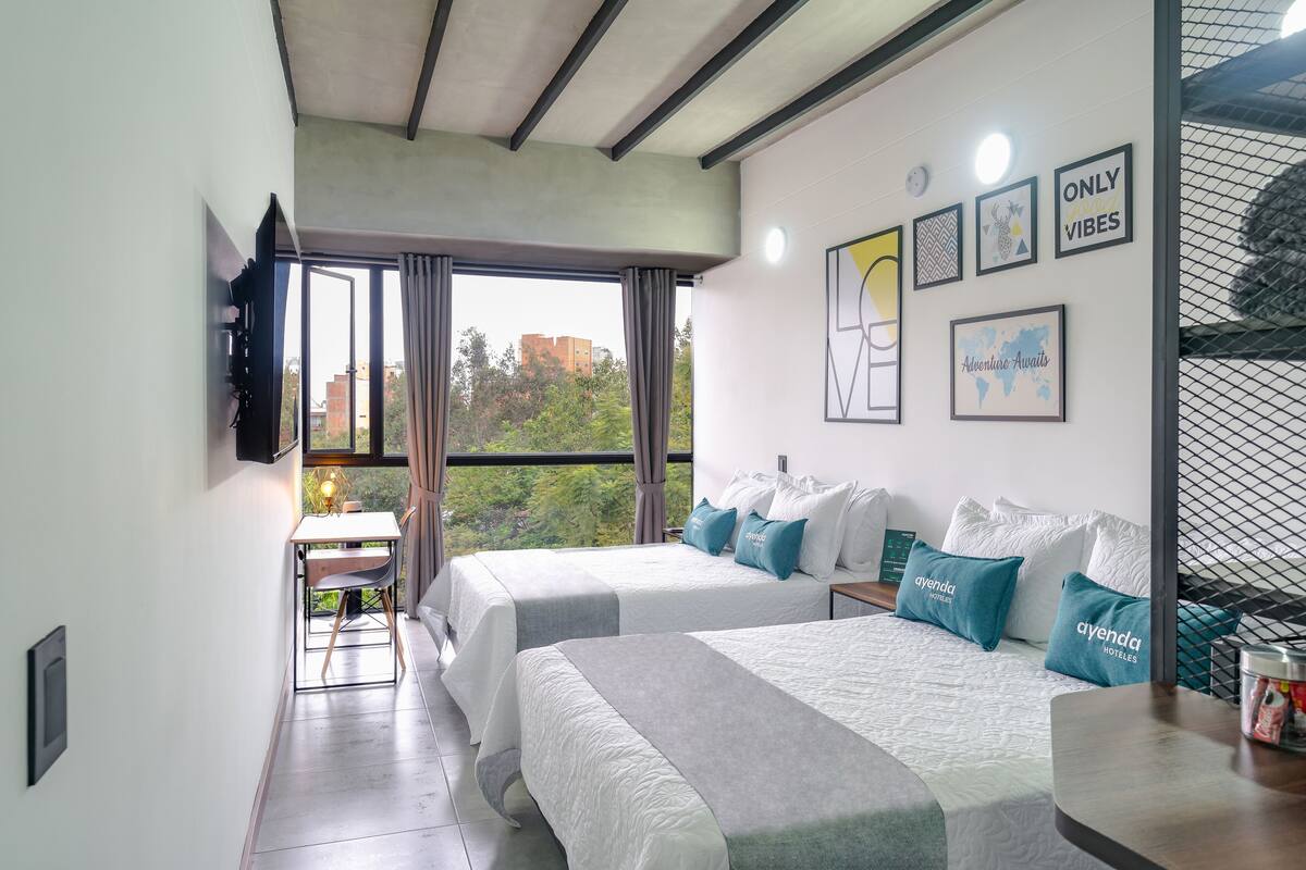 A hotel room with two beds, a desk, and a large window with curtains.