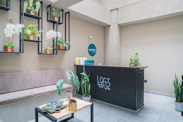 Un'area reception di un hotel dal design moderno, con una scrivania della reception, zona salotto e diverse piante in vaso.