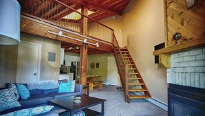 Un vaste espace de vie comprenant un salon avec une chambre en mezzanine, une cheminée et un escalier en bois.