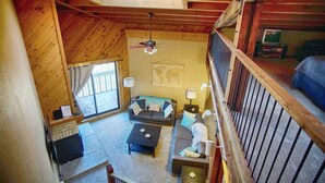 Un intérieur de chalet chaleureux avec un lit en mezzanine, un canapé, une table basse et un téléviseur.