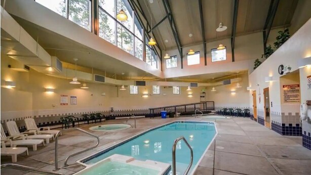 Une piscine intérieure dotée de plusieurs couloirs, baignée de lumière grâce à de grandes fenêtres et équipée de rampes de sécurité.