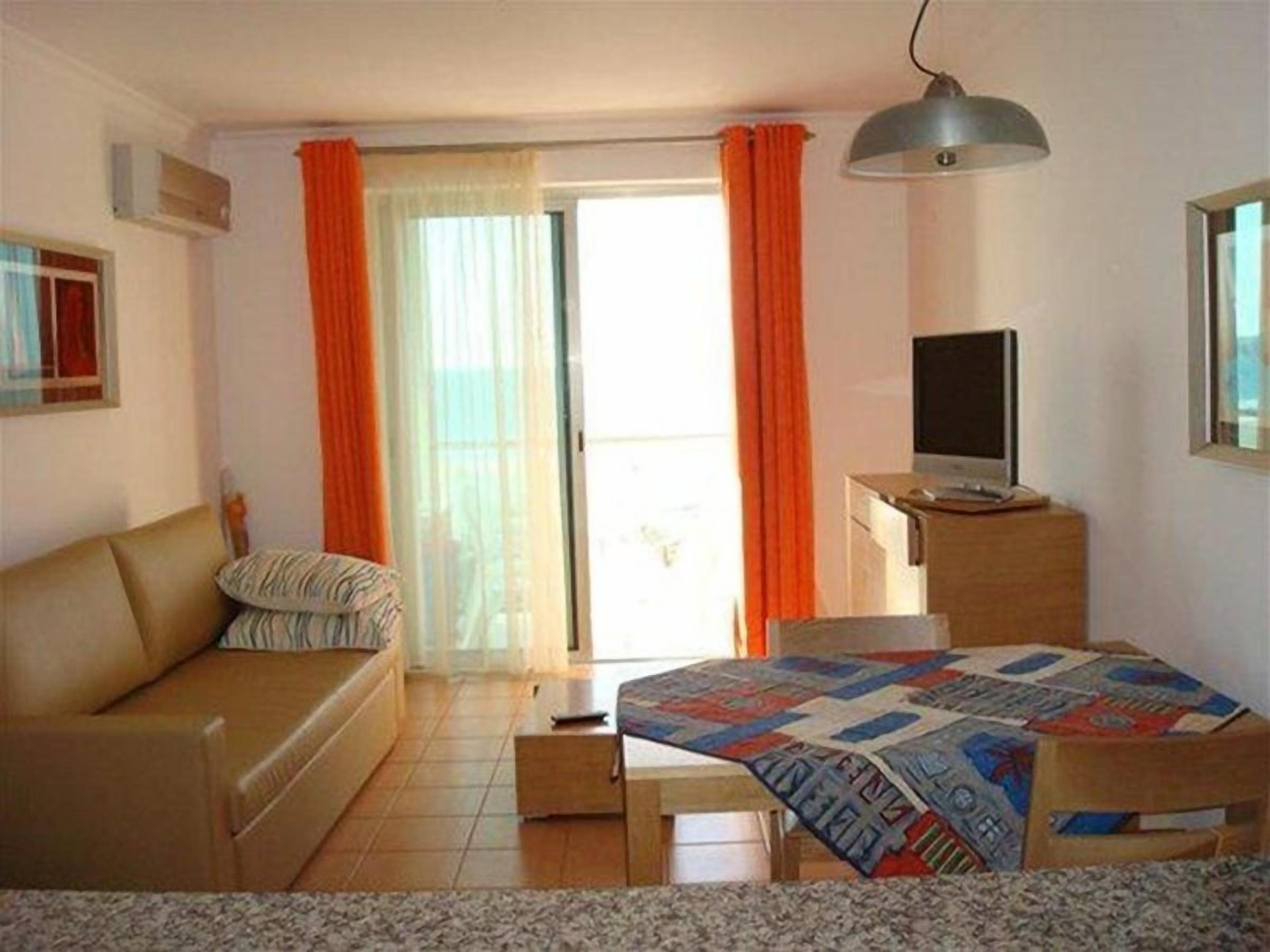 Un dormitorio con cama, escritorio, televisor y ventana con cortinas.