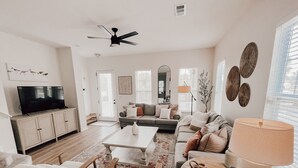 A modern living room with a flat-screen TV, a sofa, a coffee table, and a lamp. - Martinique! Luxury! Beach House on the Crescent with Golf Cart.  (Gulf Shores)