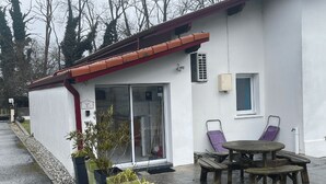 A small white building with a red roof, a sliding glass door, and a patio with a wooden table and two purple chairs. - Our gîtes are ideally located in Pontonx-sur-l'Adour (Pontonx-Sur-L'adour)