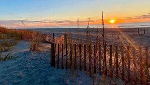 Escena de playa con una valla de madera y dunas de arena al atardecer.