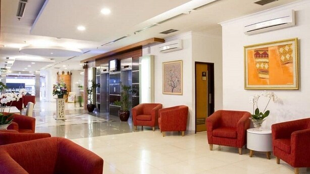 A hotel lobby with red upholstered chairs, a reception desk, and a wall-mounted air conditioning unit. - Asana Kawanua Jakarta (Jakarta)