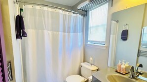 A compact bathroom with a toilet, shower curtain, and a sink with toiletries. - Cozy 3-Bdrm  Escape w/ Yard - Budget-Friendly (Austin)