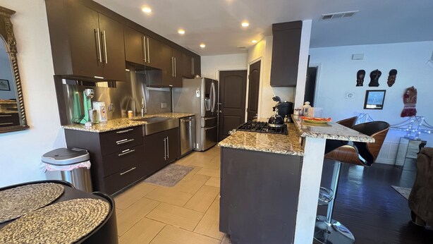 A modern kitchen with dark cabinetry, stainless steel appliances, and a granite countertop. - Cozy 3-Bdrm  Escape w/ Yard - Budget-Friendly (Austin)