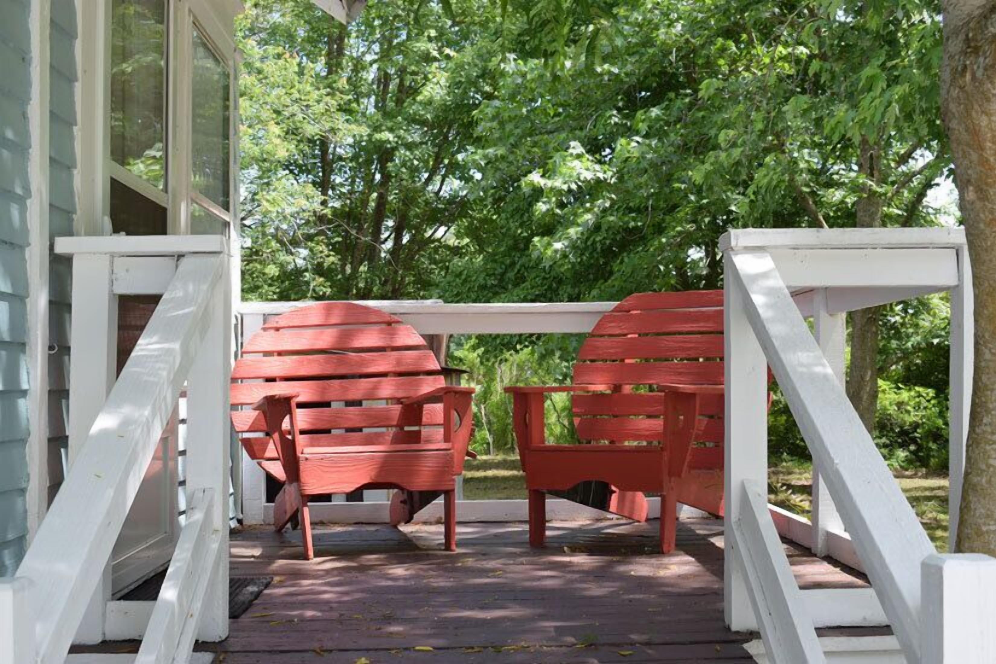 A covered porch with red Adirondack chairs and white railings.