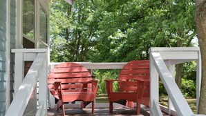 Eine überdachte Veranda mit roten Adirondack-Stühlen und weißen Geländern.