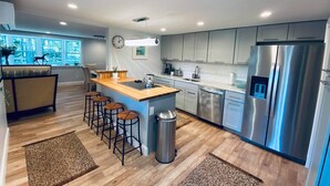 A modern kitchen with a central island, stainless steel appliances, and a view to a dining area. - Charming, newly renovated house, a few steps from bike path. (Dennis Port)
