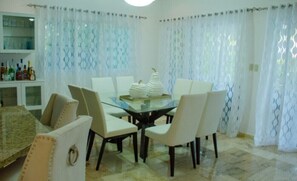 Un espace repas avec une table en verre entourée de chaises, un élément décoratif central et des rideaux à motifs.