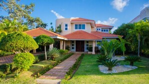 A two-story house with a red-tiled roof, a brick pathway leading to the entrance, and well-maintained greenery around the property. - Villa Esmeralda Cocotal Golf & Country (Punta Cana)