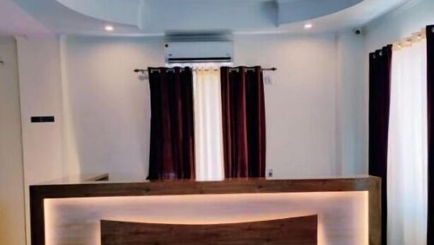 A reception desk with a wooden finish and integrated lighting, set against a white wall with a ceiling light fixture. - Deluxe family Balcony (Ramnagar)