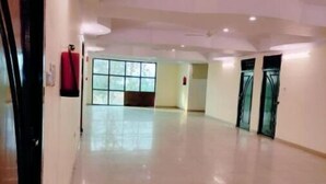 A spacious, well-lit hallway with a tiled floor, large windows, and a door with a frosted glass panel. - Deluxe family Balcony (Ramnagar)