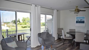 Un vaste espace de vie doté d’une grande porte-fenêtre coulissante donnant sur un balcon, d’un ventilateur de plafond et d’une table à manger avec des chaises.
