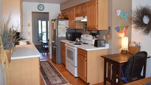 A modern kitchen with wooden cabinets, stainless steel appliances, and a dining area with a chair and table.