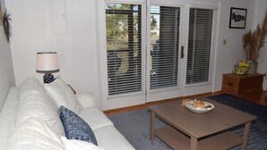 A living room with a sofa, a coffee table, and a lamp. There are two sliding glass doors with blinds.