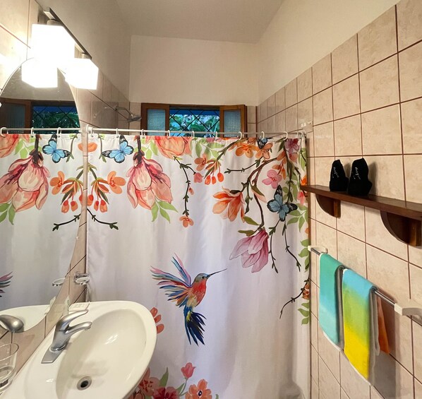 A bathroom with a floral shower curtain, a sink, and a towel rack with towels. - Latitude Adjustment, Heart of Manuel Antonio, 1BD (Quepos)