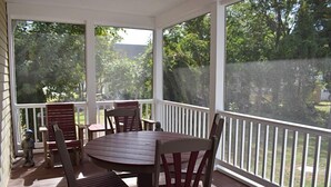 A covered outdoor patio with a wooden table and chairs, surrounded by a white railing. - 2 BR | Screened Porch | Walk to Town (Chincoteague)