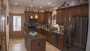 A kitchen with dark wooden cabinets, stainless steel appliances, and pendant lighting. - 2 BR | Screened Porch | Walk to Town (Chincoteague)